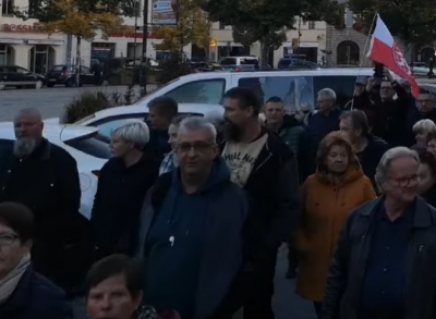 Im Halbdunkel sieht man in der Saalfelder Montagsdemo vom 3.10.2022 Christian und Jana Dietzel neben Andreas Börner laufen, alle drei blicken weg von der Kamera.