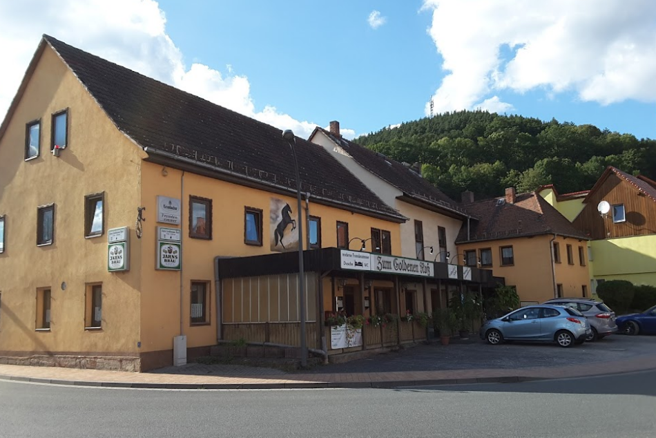 Foto des Gasthaus "Goldenes Roß" in Uhlstädt. Es ist ein größeres gelbes Haus mit Terrase und Parkplatz an einer Straße zu sehen.