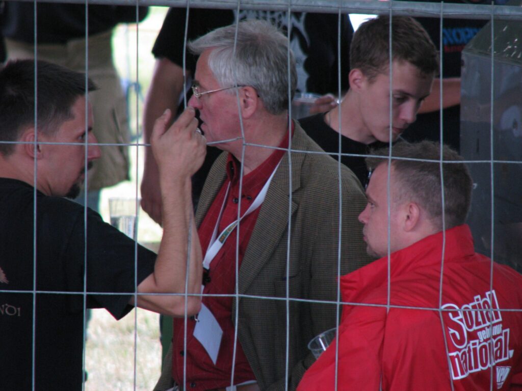 Foto einer Veranstaltung auf dem Ralf Wohlleben, Frank Schwerdt, Nico Schneider und Patrick Wieschke hinter einem Bauzaun zu sehen sind.