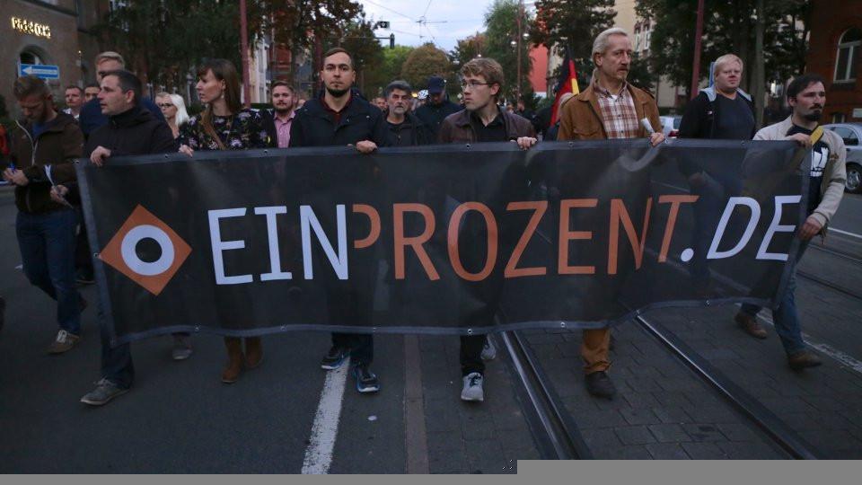 Foto von mehreren Personen auf einer Demonstration, die ein Transparent mit dem Text "EINPROZENT.DE" tragen.