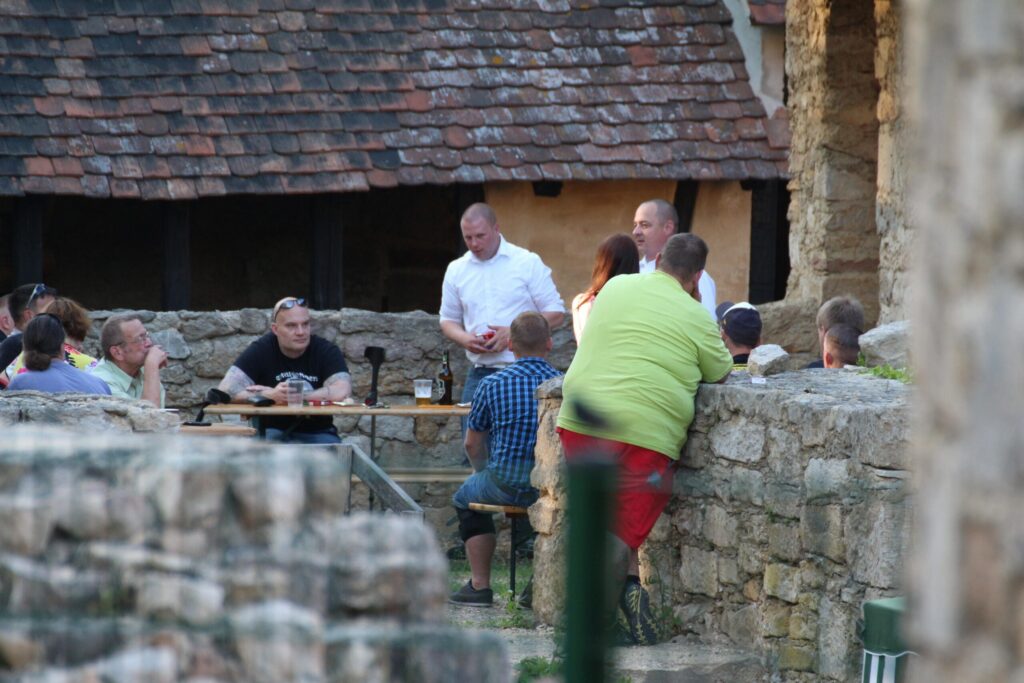 Foto von mehreren Personen. Marco Zint sitzt an einem Tisch. Martin Etzrodt und Robert Köcher stehen und referieren.