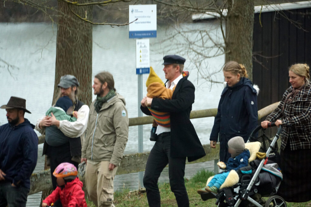Foto auf dem u.a. Nikolai Nerling, Sophia Fuchs und Janine Wöll in Pöllwitz zu sehen sind. Nerling trägt ein Kind auf dem Arm. Wöll schiebt einen Kinderwagen, in dem ein Kind sitzt.