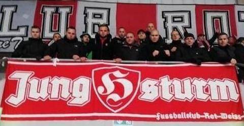 Man sieht die Jungsturm-Hooligans mit Orlin Pavlov in ihrer Mitte auf ihrem angestammten Platz im Steigerwaldstadion 2018, unter ihnen das rot-weiße Banner der Gruppe mit dem Hooligan-H in der Mitte.