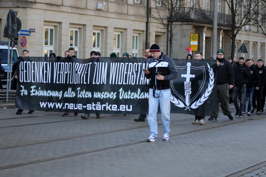 Man sieht die Spitze eines Blocks im Neonaziaufmarsch in Dresden. Auf dem Fronttransparent steht "Gedenken verpflichtet zum Widerstand. Zur Erinnerung aller Toten unseres Vaterlands." Links am Transparent sieht man Etienne Klupp.
