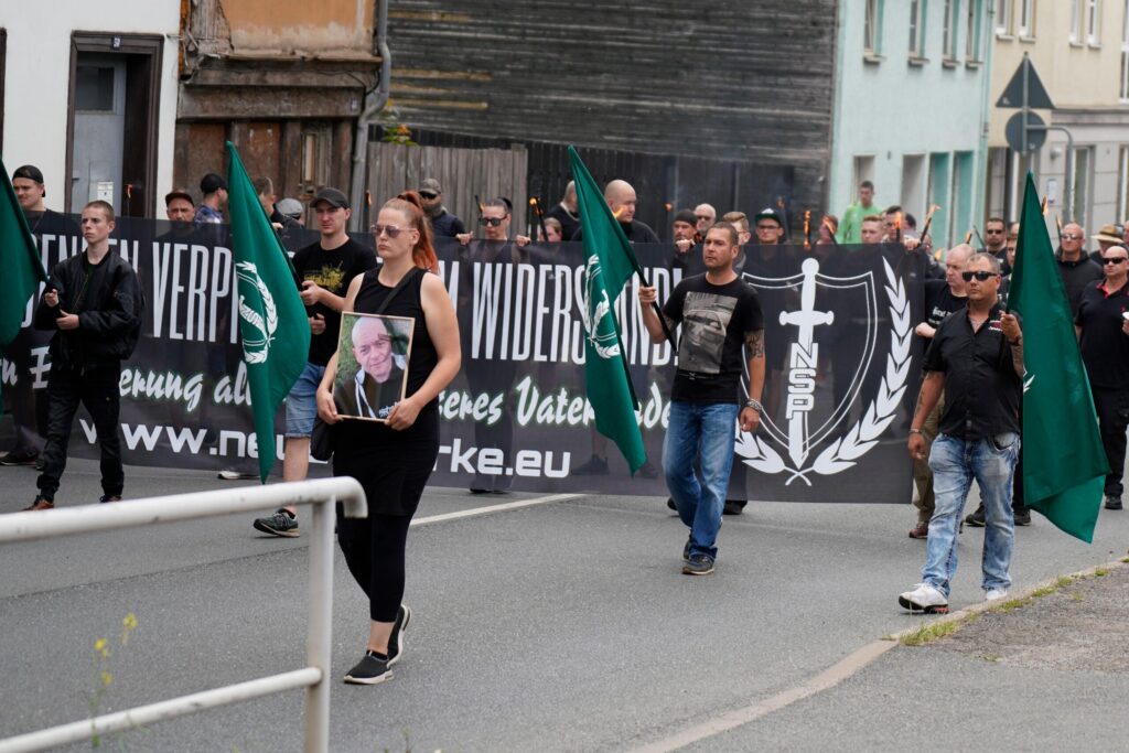 Aufmarsch mit einheitlichen grün-weißen Fahnen der Neuen Stärke und dem Fronttransparent vom Neonazi-Gedenkmarsch in Dresden. Pascal Chmielewski ist links vor dem Fronttransparent mit glatze und einer Fahne zu sehen.