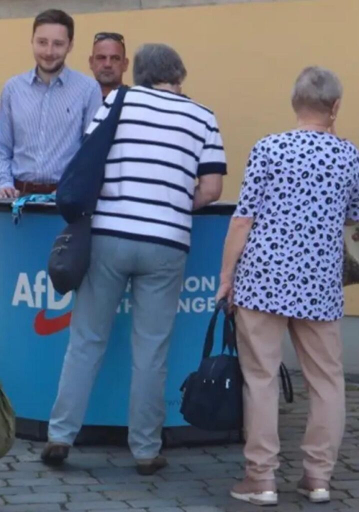 Foto von Peter Gerhardt und Marko Glaser, die hinter einem Wahlkampfstand der AfD stehen.