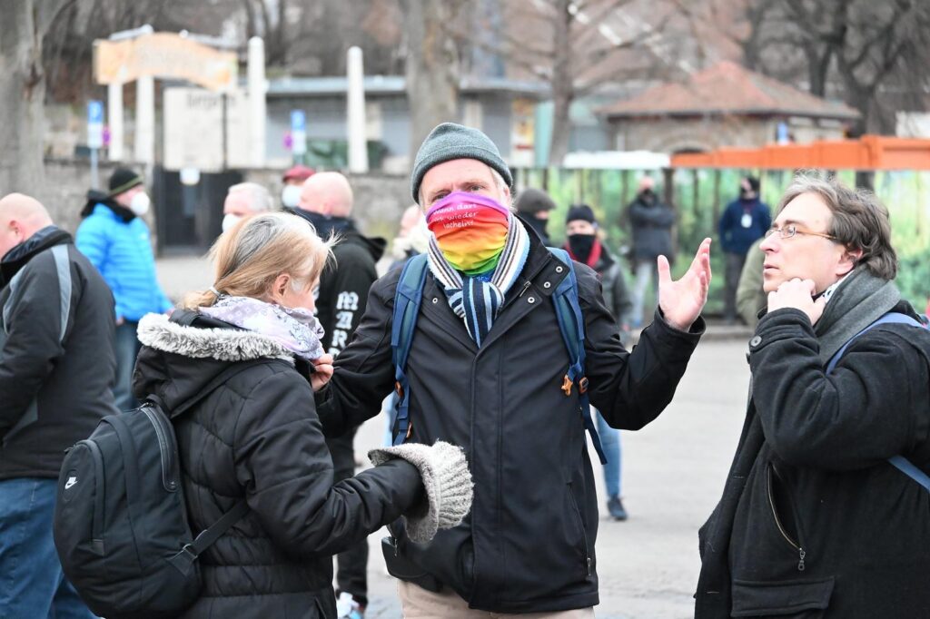 Foto von Stefan Schuster und zwei weiteren Personen bei "Thüringen steht zusammen" Demo. Schuster trägt einen regenbogenfarbenen Schlauchschal, den er über die Nase gezogen hat.