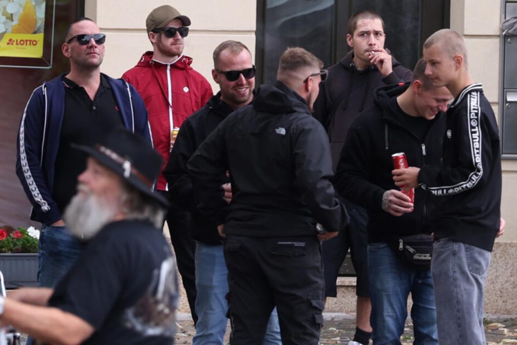 junge Männer stehen zusammen auf dem Apoldaer Markt, manche mit Sonnenbrille. Karl steht rechts mit Kurzhaarfrisur und einer Pitbull-Trainingsjacke, David Prinz trägt Sonnenbrille und eine schwarze Regenjacke