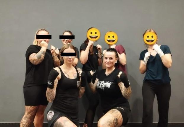 Heidi Lorber kniet vor einer Gruppe von Frauen in Boxpose. Sie trägt dabei ein schwarzes Shirt mit dem Aufdruck „One Family“. Die anderen Frauen sind durch Emojis oder schwarze Balken anonymisiert.
