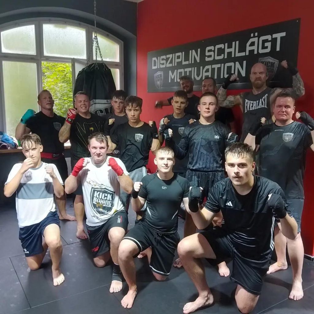 Stefan Rose ist in zweiter Reihe auf einem Gruppenfoto vom Training beim KiBo in Boxpose zu sehen. An der Wand hängt groß der Spruch: „Disziplin schlägt Motivation“